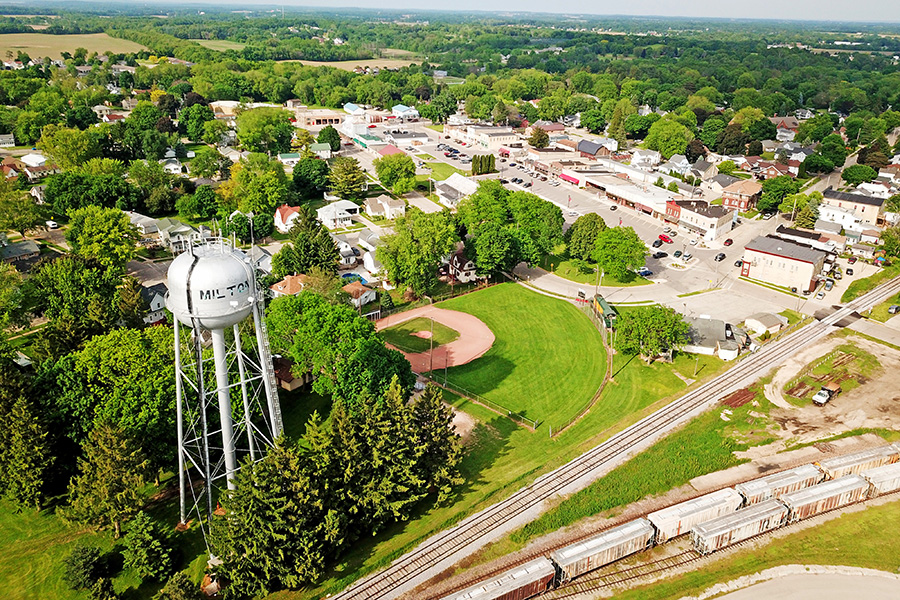 An aerial view of the City of Milton. A water tower, baseball field, train track, path, and development are all pictured. 