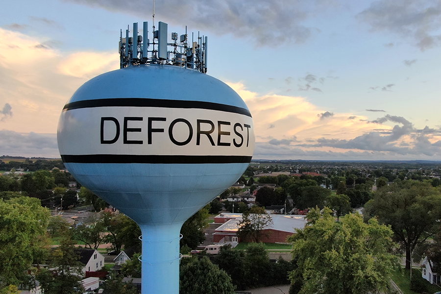 An image of a blue water tower that reads DeForest. The name of the village is in black text over a white banner background outlined in black. 