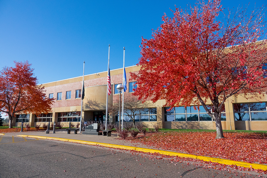 The St. Croix County Government Center is featured in this photo. A tree in fall colors is in the frame on the right. Flag poles stand outside the building.