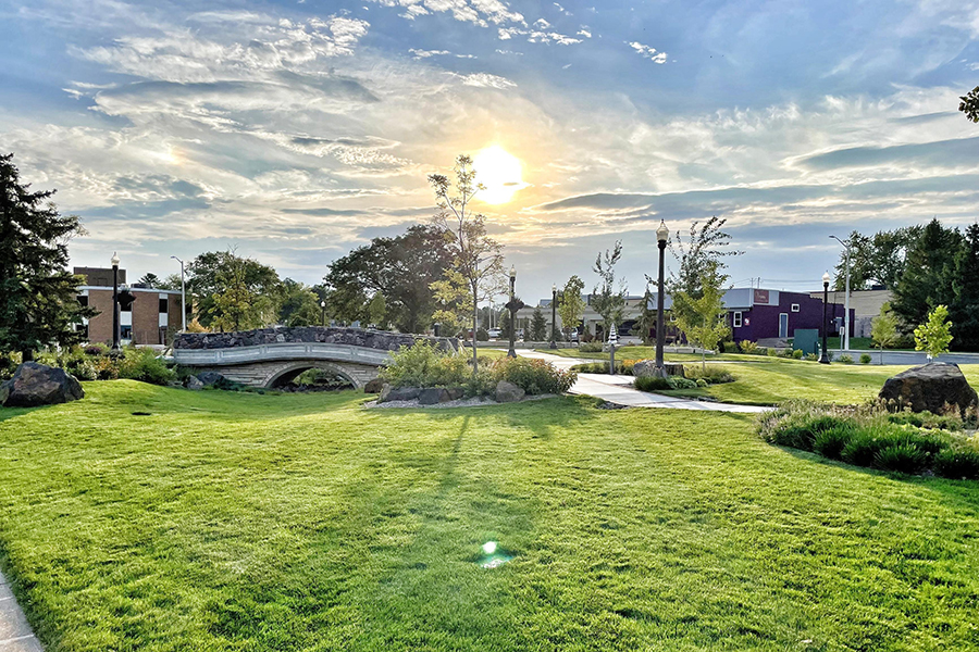Sun shines on a park in Wood County. Grass is in the foreground, and a bridge is in the background.