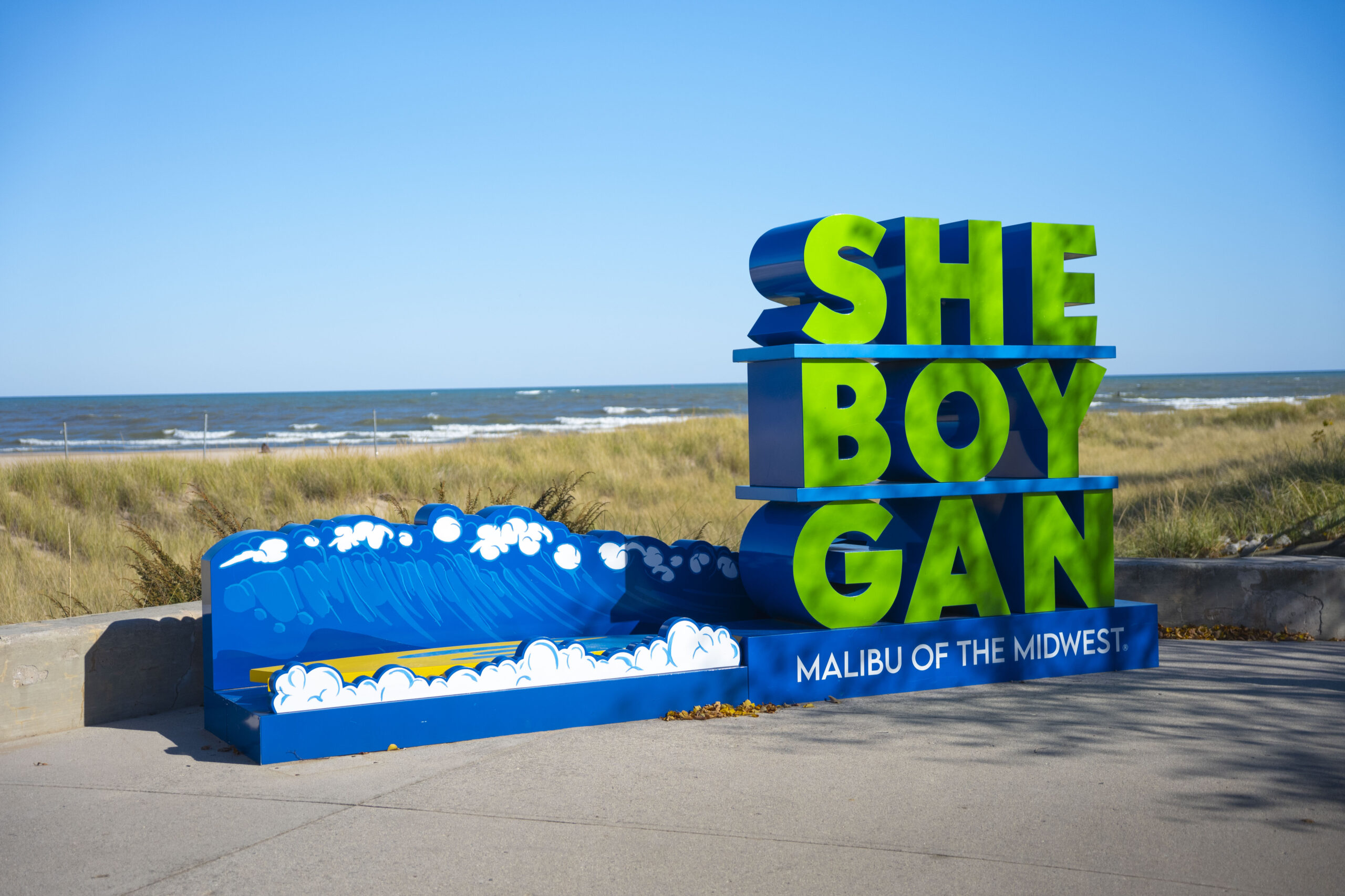 A tourism sign that readhs Sheboygan in block letters with the tag lane: Malibu of hte Midwest. Lake Michigan is in the background.