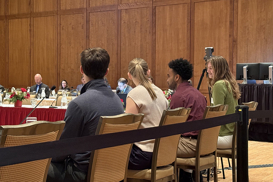 Four students sit in a row at a table while discussing learning experiences at a panel. 